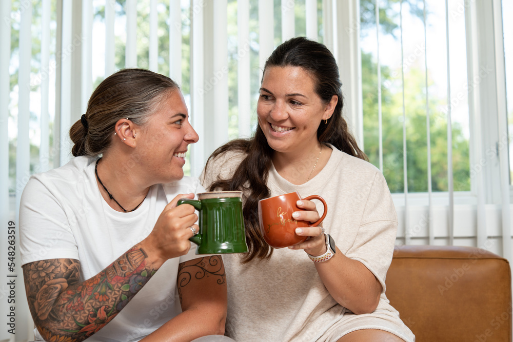 Adult lesbian couple sit on couch with coffee at home Adult lesbian couple sit on couch with coffee at home