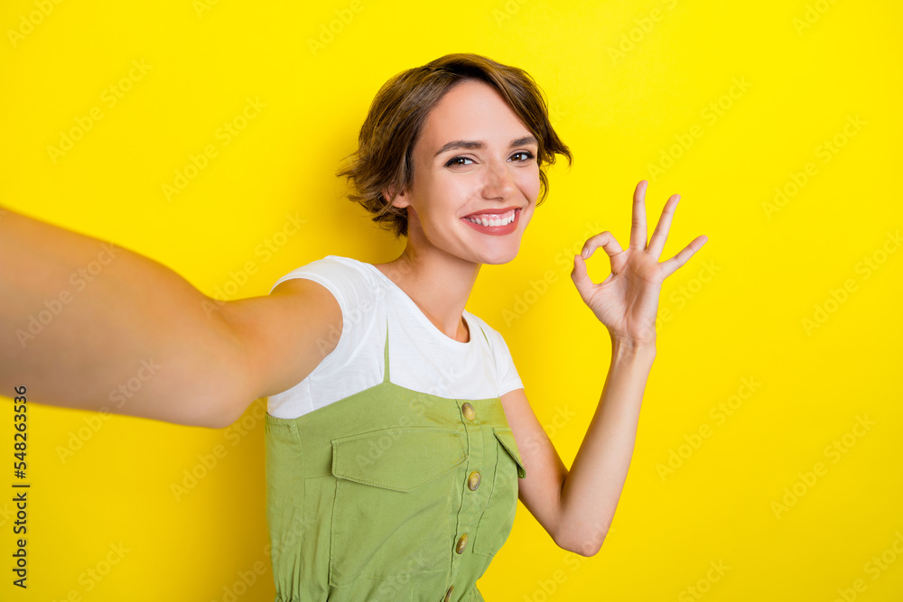 Closeup selfie photo of youngster woman toothy beaming smile showing okey sign recommend new brand isolated on yellow color background Closeup selfie photo of youngster woman toothy beaming smile showing okey sign recommend new brand isolated on yellow color background