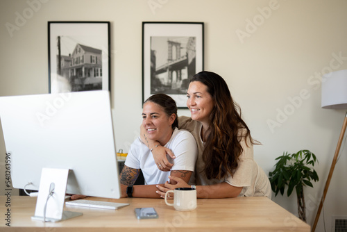 Adult lesbian couple use desktop computer in home office