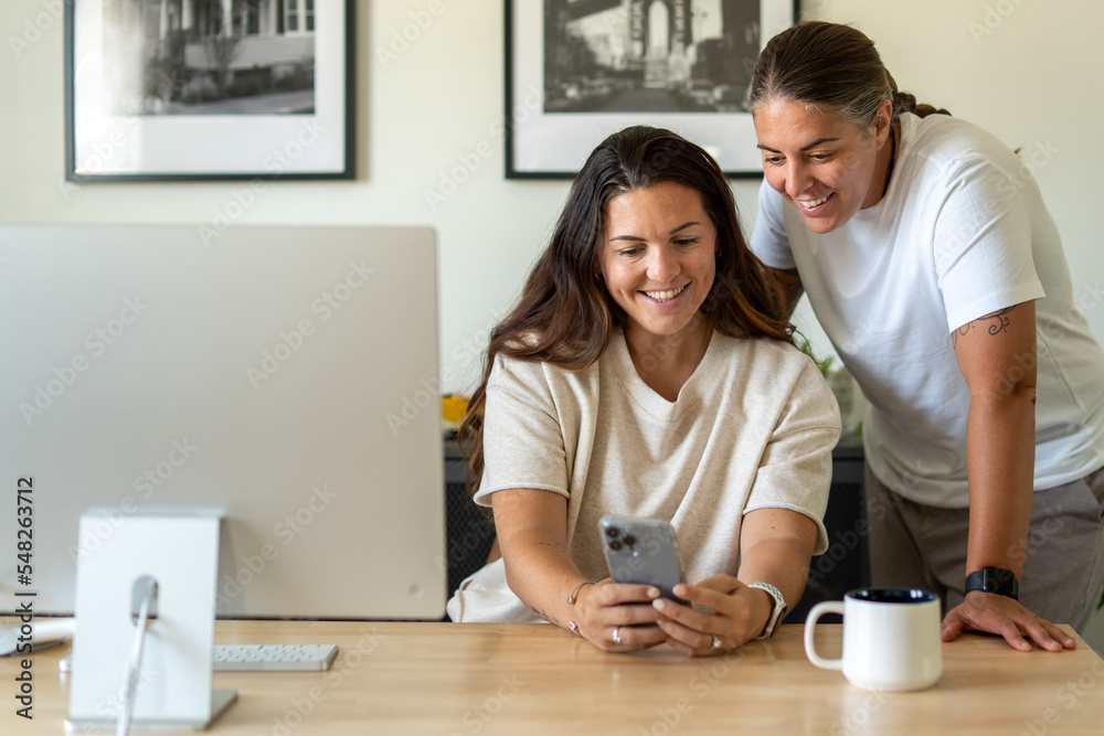 Adult lesbian couple use phone in home office Adult lesbian couple use phone in home office