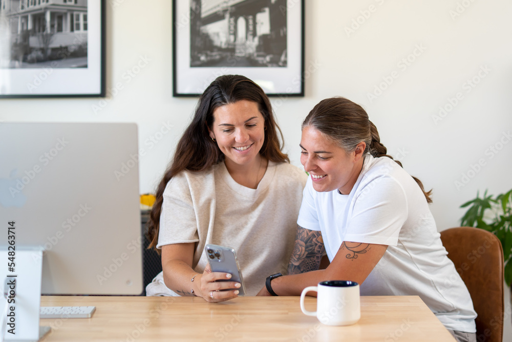 Adult lesbian couple use phone in home office Adult lesbian couple use phone in home office