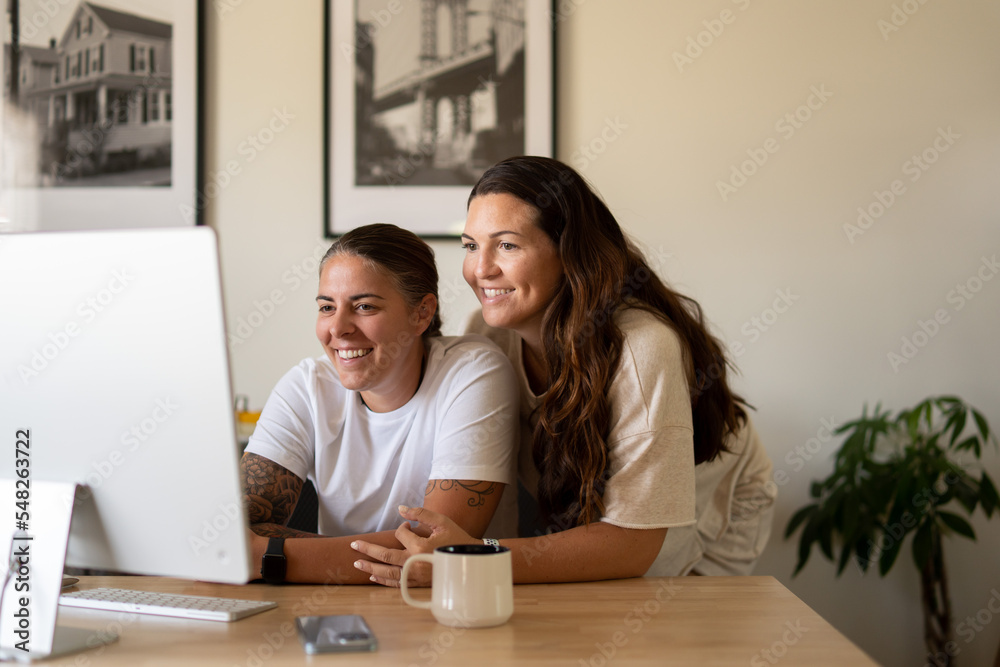 Adult lesbian couple use desktop computer in home office Adult lesbian couple use desktop computer in home office