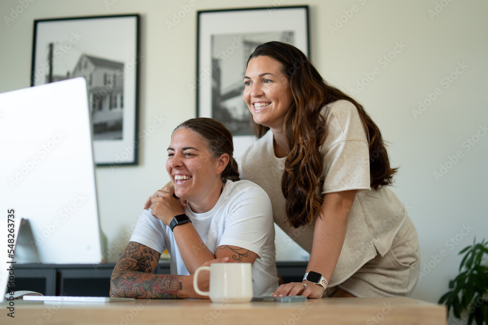 Adult lesbian couple use desktop computer in home office Adult lesbian couple use desktop computer in home office