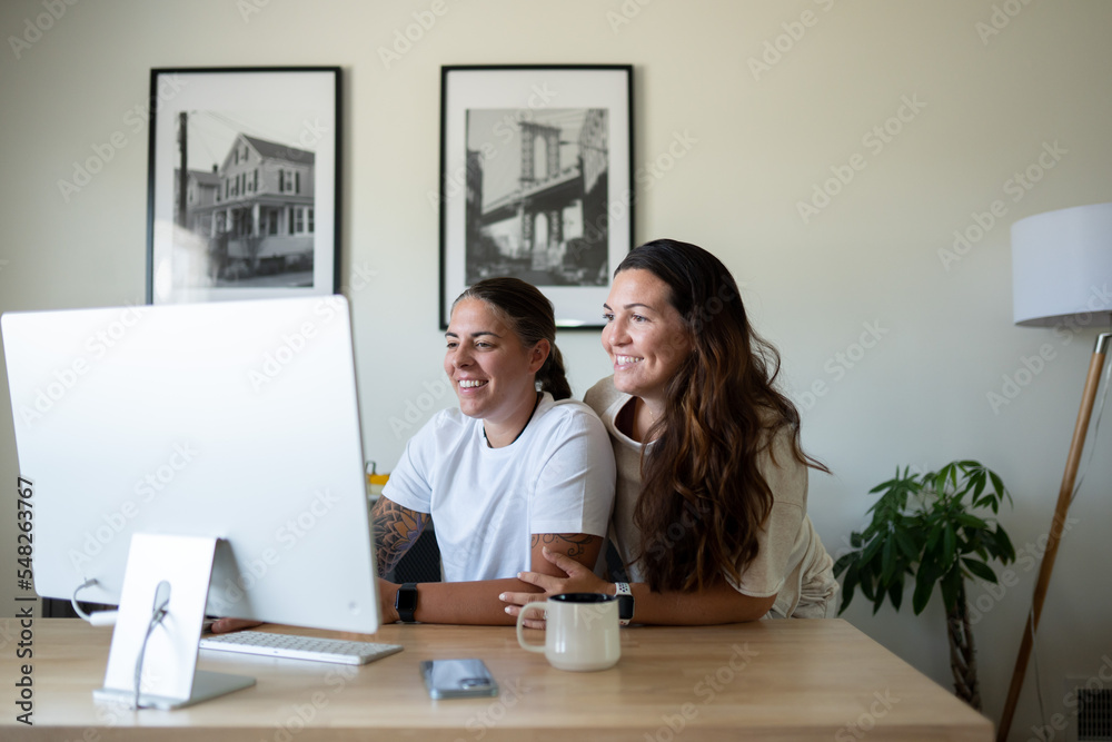 Adult lesbian couple use desktop computer in home office Adult lesbian couple use desktop computer in home office