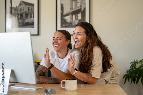 Adult lesbian couple use desktop computer in home office for video call