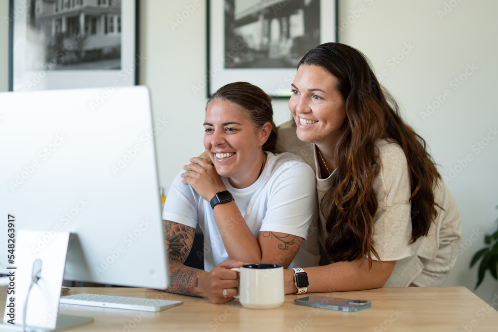 Adult lesbian couple use desktop computer in home office Adult lesbian couple use desktop computer in home office