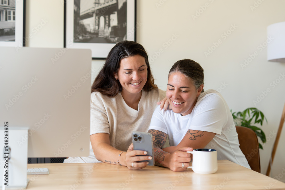 Adult lesbian couple use phone in home office Adult lesbian couple use phone in home office