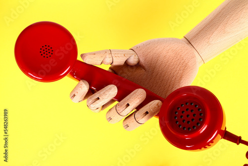 Wooden hand holding a red old fashioned retro telephone handset photo