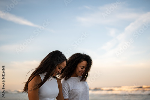 Hispanic lesbian couple walk at the beach holding hands