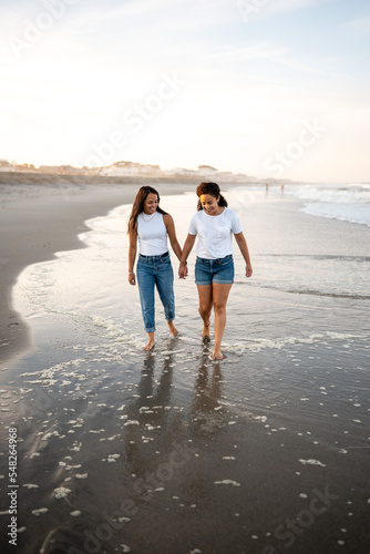 Hispanic lesbian couple walk in the water at the beach holding hands