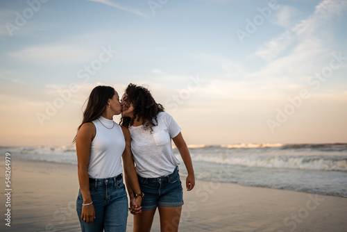Hispanic lesbian couple kiss and walk in the ocean at the beach