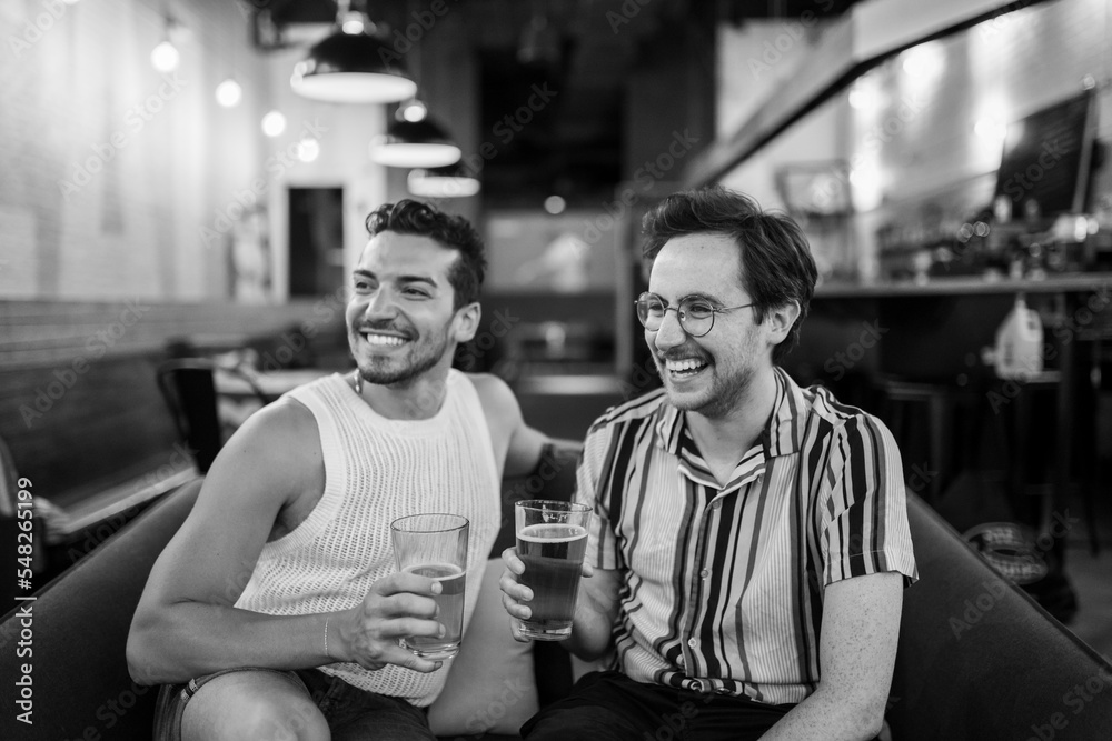Two LGBTQ friends drink beer on a couch Two LGBTQ friends drink beer on a couch