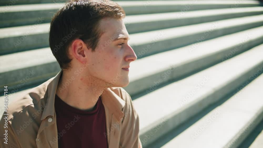 Young man portrait. Happy guy smiling close-up. Male cheerful student model posing, sitting on stairs outdoor, looking at camera. Young man portrait. Happy guy smiling close-up. Male cheerful student model posing, sitting on stairs outdoor, looking at camera.