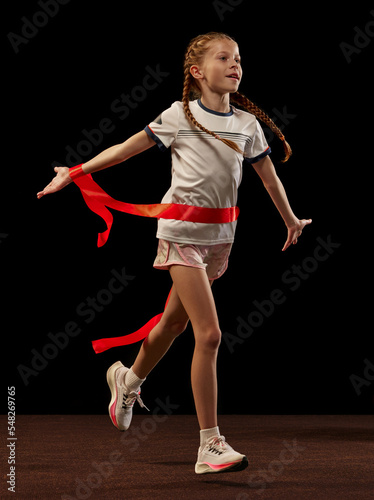 Successfully finishing race. Happy female junior runner in sportswear isolated on dark background. Concept of sport, fashion, fitness and education