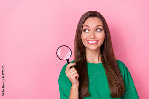 Photo of gorgeous adorable pretty girl dressed green t-shirt look empty space hold magnifying glass isolated on pink color background © deagreez