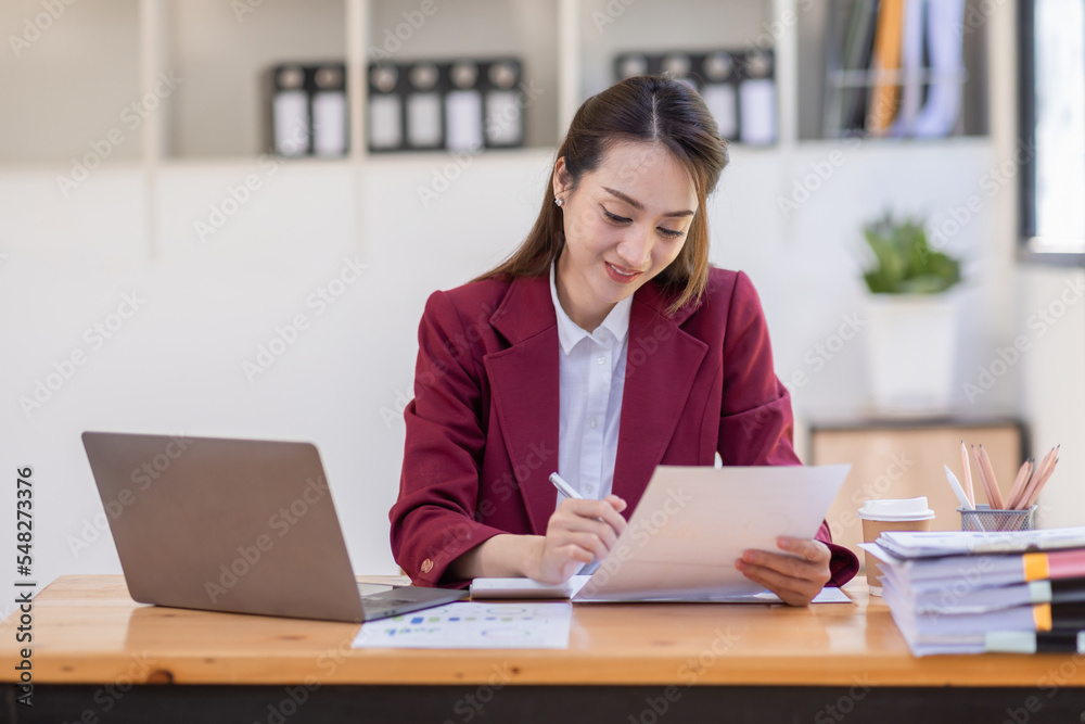 Asian woman working laptop in workplace, Business woman wearing red jacket suit busy working on laptop computer checking finances, investment, economy, saving money or insurance concept Asian woman working laptop in workplace, Business woman wearing red jacket suit busy working on laptop computer checking finances, investment, economy, saving money or insurance concept