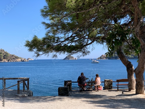 Summer landscape in Turkey near Marmaris. View of the bay and mountains through pine branches. Couple on the bench.