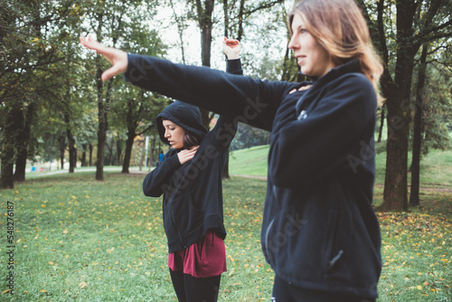 Two active sportive women stretching outdoors park wearing hoodie