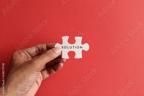 Hand holding puzzle pieces with text SOLUTION on red background. Top view with copy space
