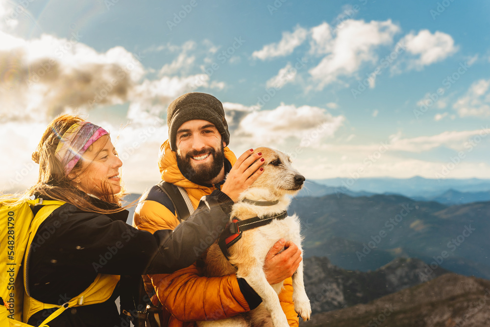 couple of hikers doing a mountain route with their dog. Mountaineer holding his dog in his arms with a mountain range landscape in the background. woman petting dog