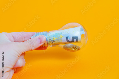Light bulb with money in hand on yellow