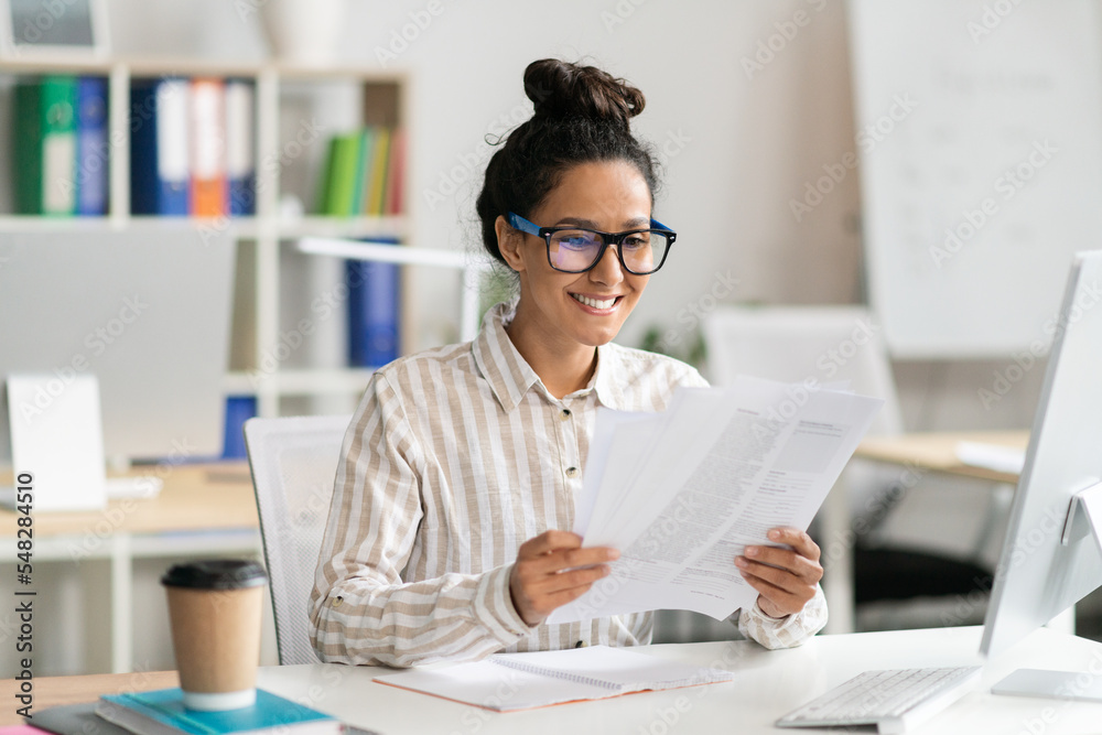 Happy businesswoman working with papers at desk in office, positive female entrepreneur reading financial documents Happy businesswoman working with papers at desk in office, positive female entrepreneur reading financial documents