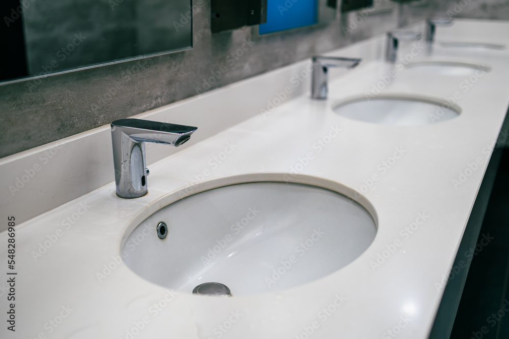 a row of washstands in a public toilet, an automatic water faucet a row of washstands in a public toilet, an automatic water faucet
