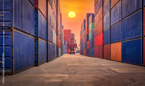 Shipping container site loading by crane in logistic port warehouse storage with cargo container background at sunset. Logistics global import or export shipping industrial concept.