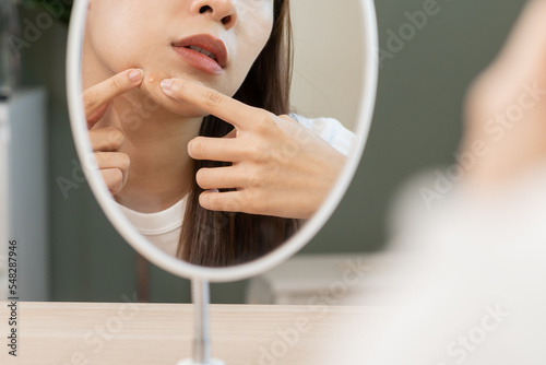 Expression worry asian young woman hand touching pustule around the chin and mouth, allergic when wear mask, makeup, show squeezing pimple spot from face. Beauty care, skin problem by acne treatment.