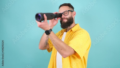 Crazy emotions. Young funny hipster tourist looking through a spyglass and considering the sights isolated on studio background. Looking for discounts, sale, seasonal sales. Colorful summer concept. photo