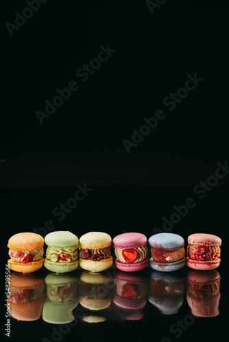 A set of large macaroons of different colors and different fillings. On a black isolated background. Macaroons in a row.