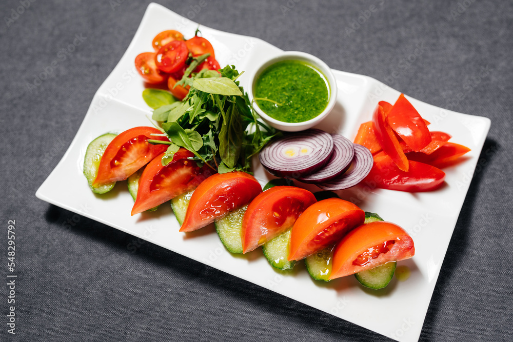Vegetables, cut into circles, on a plate, sprinkled with greens and green paste. Tomatoes, cucumbers, peppers and arugula.