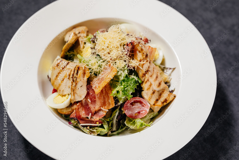 Caesar salad on a white plate, decorated with cheese, with chicken and tomatoes. Restaurant concept. Caesar salad on a white plate, decorated with cheese, with chicken and tomatoes. Restaurant concept.