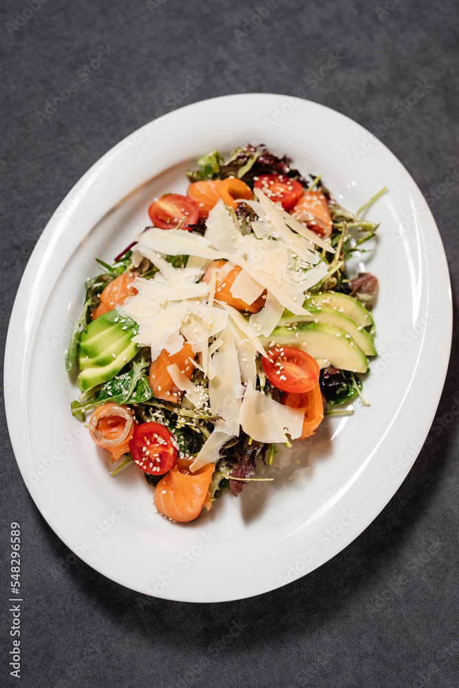 Salad with avocado and salmon on a white plate, decorated with parmesan slices. Restaurant concept. Salad with avocado and salmon on a white plate, decorated with parmesan slices. Restaurant concept.