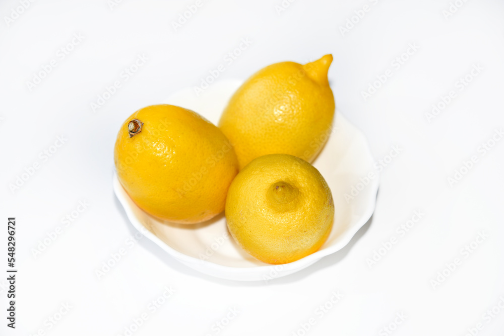 Yellow juicy lemons in a white saucer. Delicious yellow lemons on a white background. Beautiful lemons on a plate.