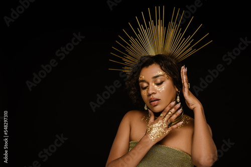 pretty african american woman with golden accessories and paint on face posing isolated on black.