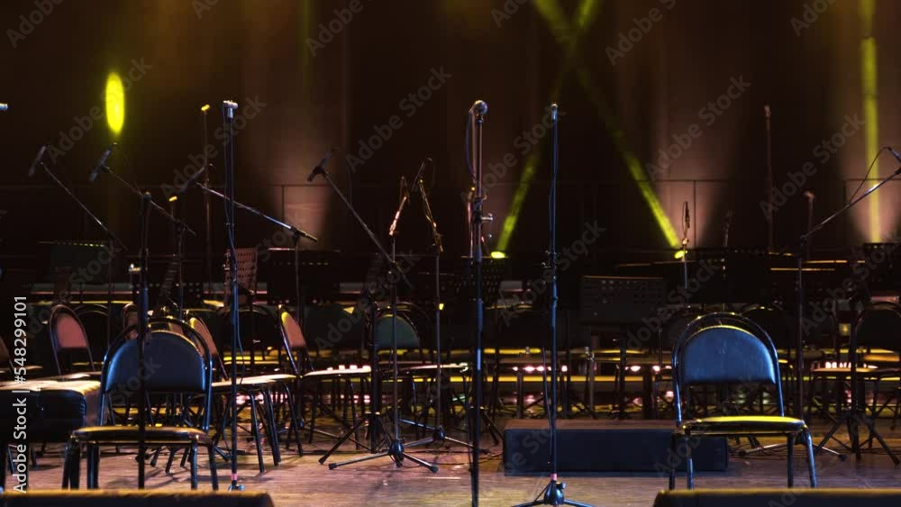 Concert light. Stage lighting background. An empty stage and a hall without people. There are a lot of empty chairs and microphones on the stage for musicians.