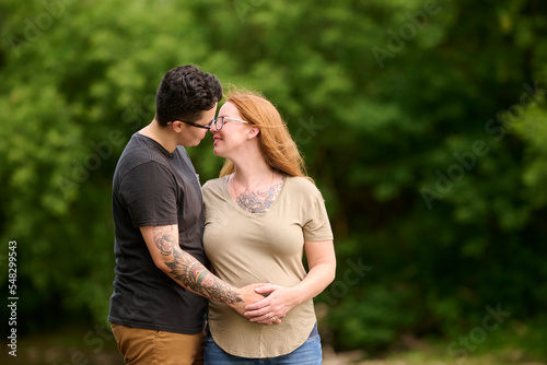 Female holding same sex partners pregnant stomach outdoors.