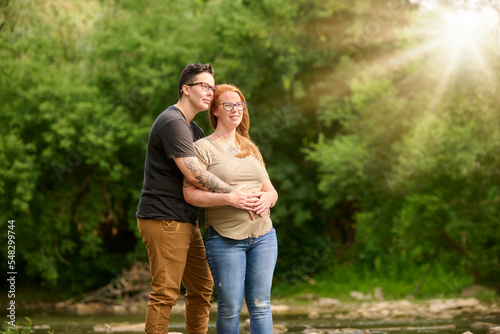 Female holding same sex partners pregnant stomach outdoors.