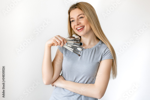 Portrait of a makeup artist girl on a white background, she is holding a makeup brushes. Copy space. Place for text.