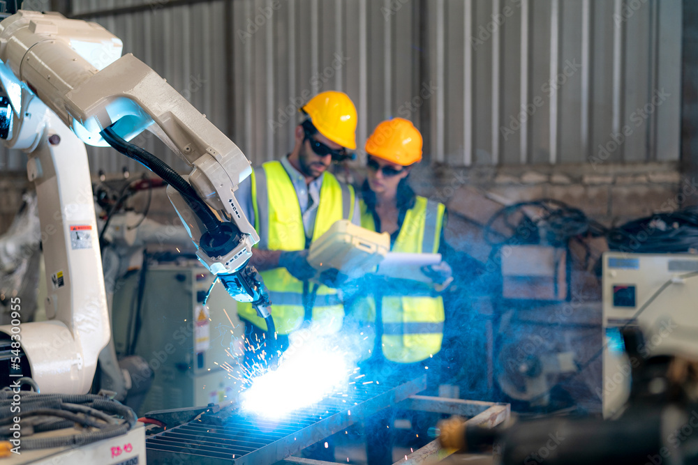 Fototapeta premium Robotics engineer working on maintenance of modern robotic arm in factory warehouse
