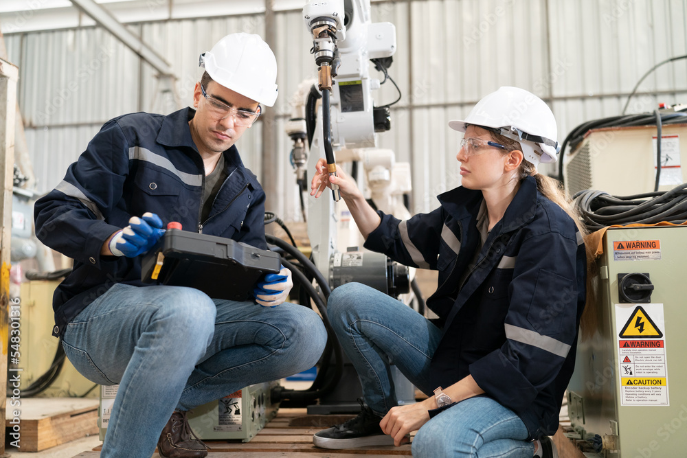 Robotics engineer working on maintenance of modern robotic arm in factory warehouse Robotics engineer working on maintenance of modern robotic arm in factory warehouse
