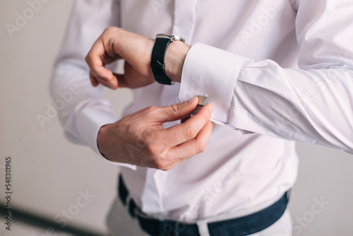 the man wears silver cufflinks on the cuff of a white shirt. The groom's hands fasten the cufflinks to the sleeve. Groom's morning
