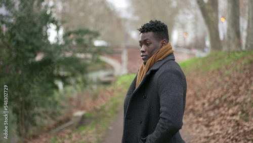Serious black African man standing at park wearing winter clothing thinking about life