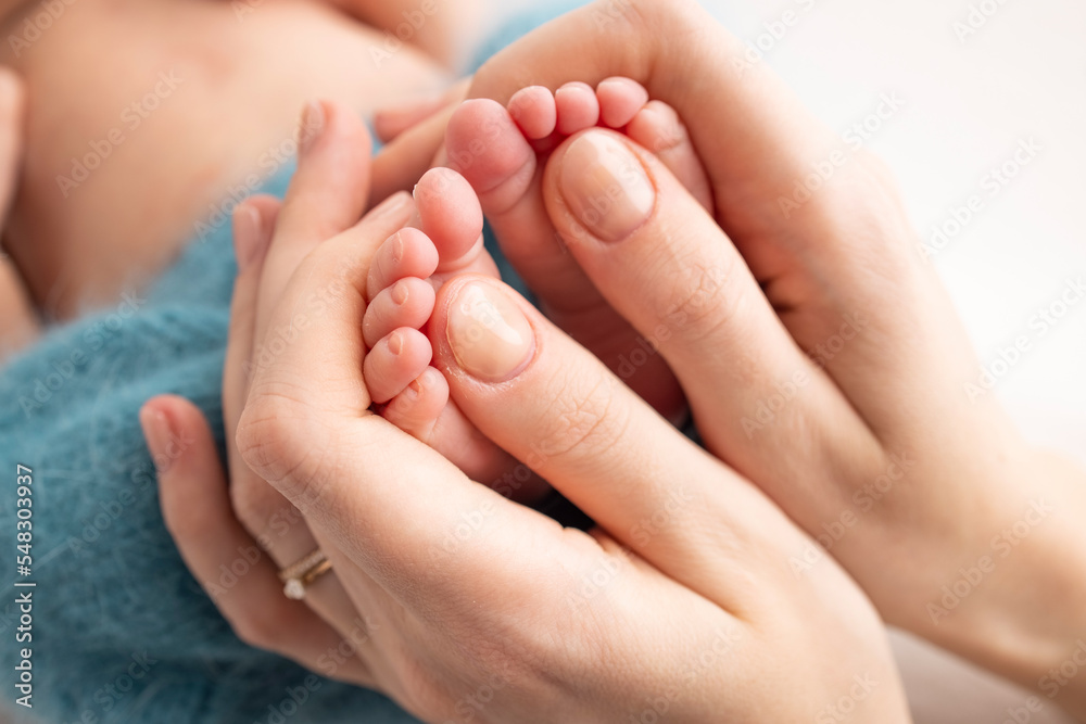 Mother is doing massage on her baby foot. Close up baby feet in mother hands on a blue background. Prevention of flat feet, development, muscle tone, dysplasia. Family, love, care, and health concept Mother is doing massage on her baby foot. Close up baby feet in mother hands on a blue background. Prevention of flat feet, development, muscle tone, dysplasia. Family, love, care, and health concept