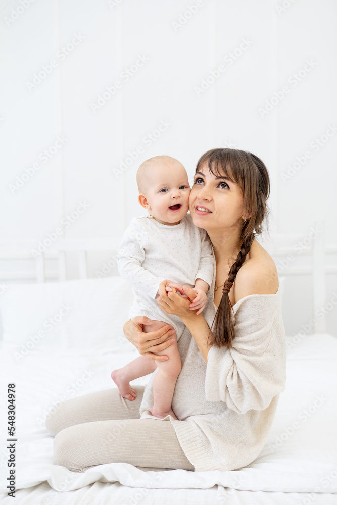 happy mom with a baby daughter at home on the bed hugs and kisses, happy young mother and motherhood happy mom with a baby daughter at home on the bed hugs and kisses, happy young mother and motherhood
