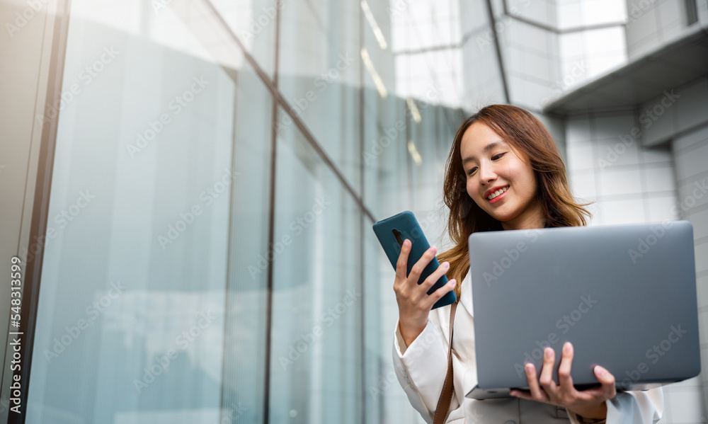 Confident businesswoman using smart phone with computer laptop standing in the city. Beautiful businesswoman being ready to work. Business concept. Confident businesswoman using smart phone with computer laptop standing in the city. Beautiful businesswoman being ready to work. Business concept.