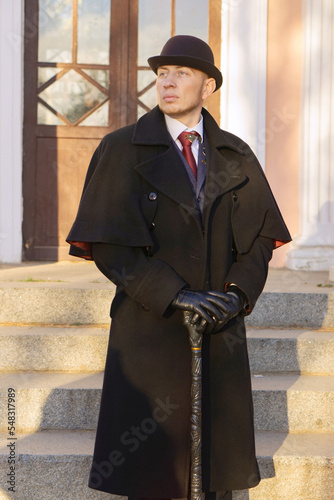 A young respectable man in a vintage coat, suit, bowler hat and with a cane