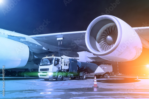 Photography Process of aircraft refueling using a tanker truck connected to the fuel tanks of the aircraft with hoses at night airfield