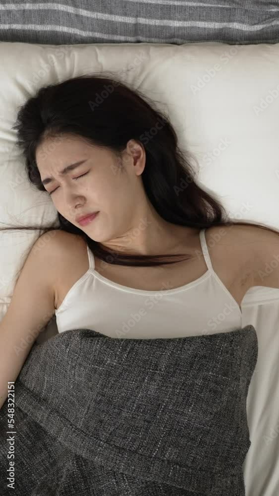 Vertical Screen: top angle view of tired asian girl continue to sleep in after hand searching and hitting electric snooze alarm, unable to wake up in the morning on bed at home Vertical Screen: top angle view of tired asian girl continue to sleep in after hand searching and hitting electric snooze alarm, unable to wake up in the morning on bed at home